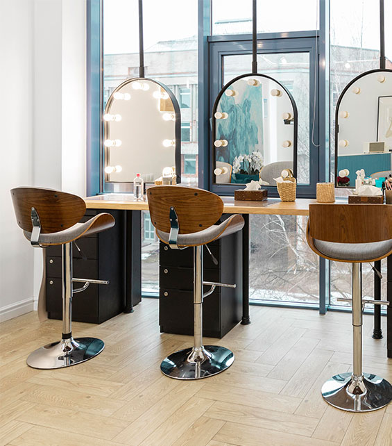 A row of 3 training stations set up, complete with seats and mirrors, in a well-lit and fashionable beauty training centre.