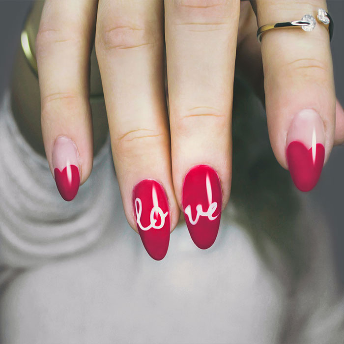 A woman's painted fingernails in red, with her middle two fingernails stylised further with the word 'love' inscribed, as part of a builder gel nail course in Manchester.